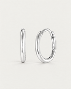 The Kiri Huggie Hoops — upright silver pair, front/edge-on and three-quarter views on pale greige; reference-based AI visualization.