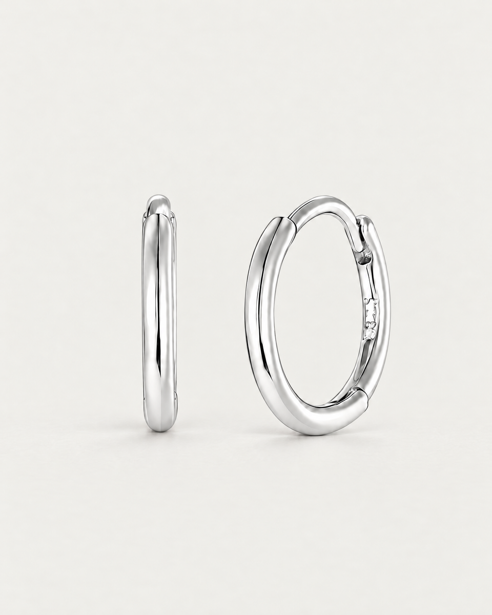 The Kiri Huggie Hoops — upright silver pair, front/edge-on and three-quarter views on pale greige; reference-based AI visualization.