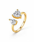 The Nessa Heart & Pear Ring in polished yellow-gold-tone metal with clear faceted heart and pear stones, shown complete in a front three-quarter pearl-white studio view — reference-based AI visualization.