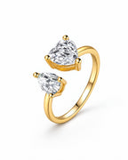 The Nessa Heart & Pear Ring in polished yellow-gold-tone metal with clear faceted heart and pear stones, shown complete in a front three-quarter pearl-white studio view — reference-based AI visualization.