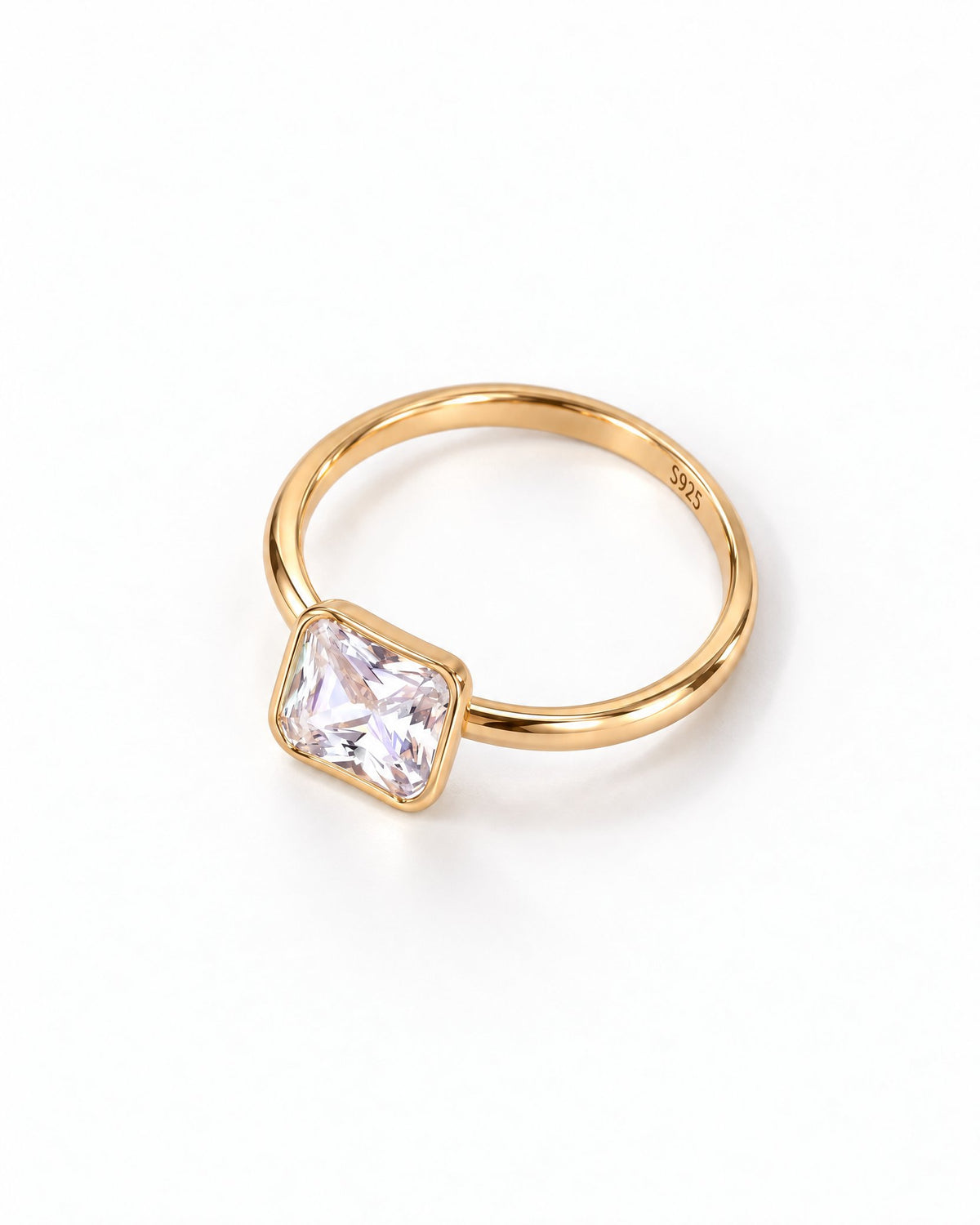 The gold-finish Eira Square Solitaire Ring shown complete at an overhead resting angle on pearl white with its single clear square stone and smooth bezel; reference-based AI visualization.