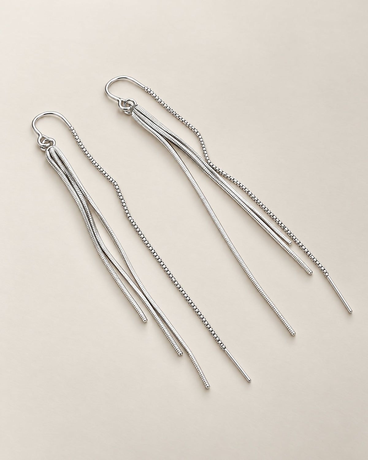 The Neri Threader Earrings, paired bright silver-tone threaders in a diagonal overhead arrangement on pale greige, reference-based AI visualization