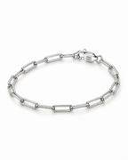 The Aelin Paperclip Bracelet in polished silver tone, complete oval resting lay with the marked clasp toward the upper-right on a plain pearl-white studio surface; reference-based AI visualization