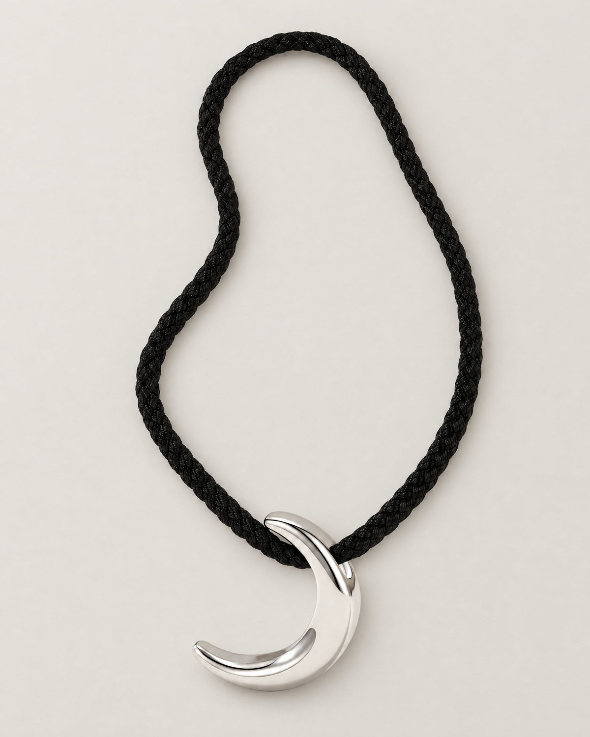 Black braided cord in a tall asymmetric loop with a polished crescent pendant at its base on pale greige, reference-based AI visualization