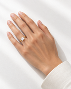 The gold-finish Eira Square Solitaire Ring worn naturally on an adult hand with an ivory cuff against a light neutral background; reference-based AI visualization.