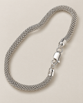 The Liva Mesh Chain Bracelet in silver-tone woven mesh, shown as a full three-quarter loop with lobster clasp and visible 925 ITALY end-cap marking on warm pale greige; reference-based AI visualization.