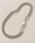 The Liva Mesh Chain Bracelet in silver-tone woven mesh, shown as a full three-quarter loop with lobster clasp and visible 925 ITALY end-cap marking on warm pale greige; reference-based AI visualization.