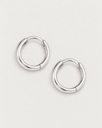 The Kiri Huggie Hoops — silver pair — separated overhead lay on pale greige, product-only; reference-based AI visualization.