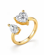 The Nessa Heart & Pear Ring in polished yellow-gold-tone metal with clear faceted heart and pear stones, shown complete in a setting-depth pearl-white studio profile — reference-based AI visualization.