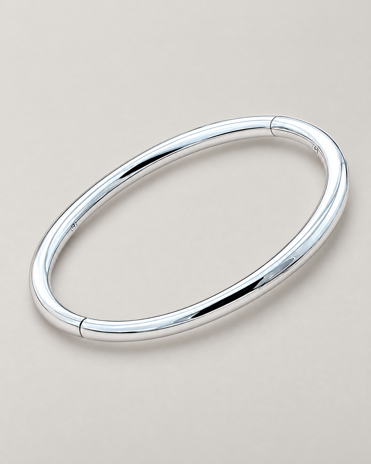The Talo Open Cuff Bangle — polished silver-tone closed oval diagonal resting lay on pale greige; reference-based AI visualization