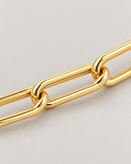 The Linnea Link Bracelet — polished gold-color interlocked paperclip-link macro on pale greige — reference-based AI visualization
