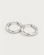 The Kiri Huggie Hoops — silver pair — low-angle overlapping lay on pale greige, product-only; reference-based AI visualization.