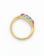 The Miri Color-Accent Band with a polished yellow-gold-colored band, three light-blue round stones and two magenta round accent stones, complete high-angle face-up view on a pearl-white studio background, reference-based AI visualization