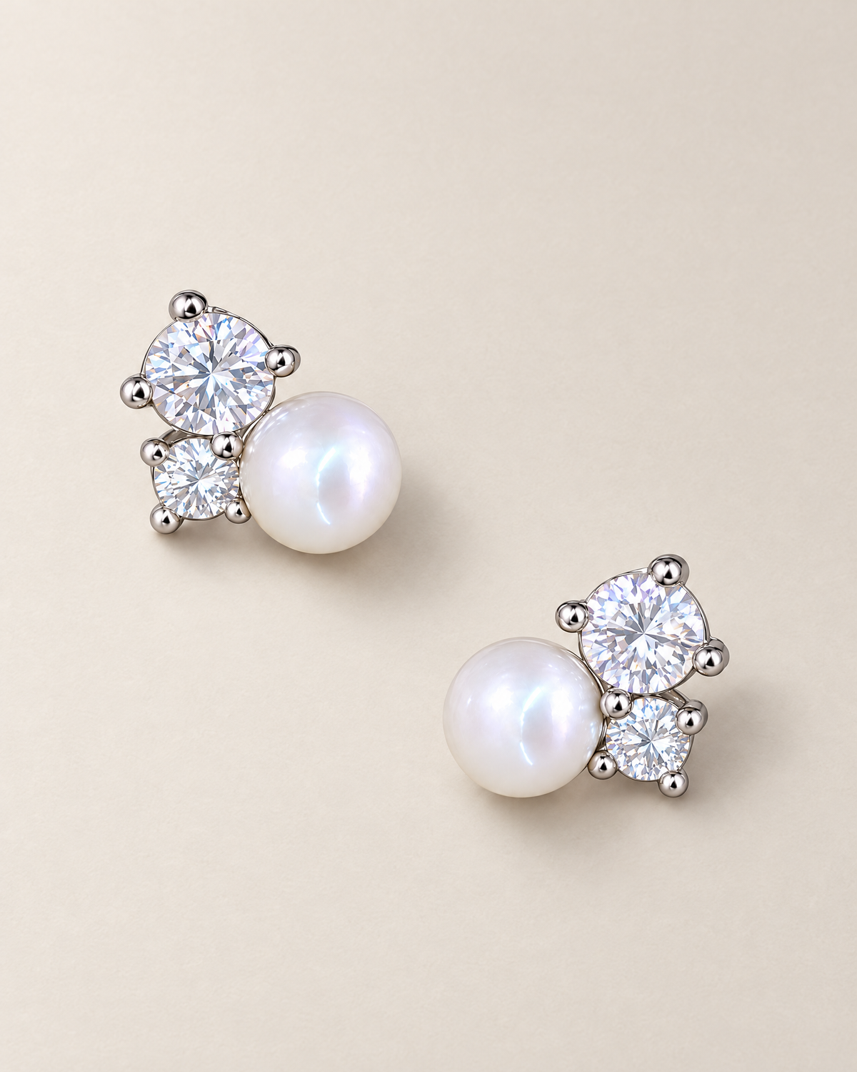 The Elva Pearl & Moissanite Stud Earrings, separated overhead pair of silvery studs with white pearls and clear round stones on pale greige, reference-based AI visualization.
