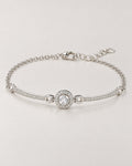 The Sora Halo Bracelet polished cool silver-tone complete shallow-oval hero with clear-stone halo, curved stone-set bars, fine chain and open-link extension on pale greige reference-based AI visualization