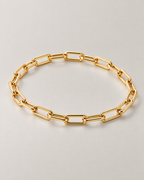 The Linnea Link Bracelet — polished gold-color oblique paperclip-link oval on pale greige — reference-based AI visualization