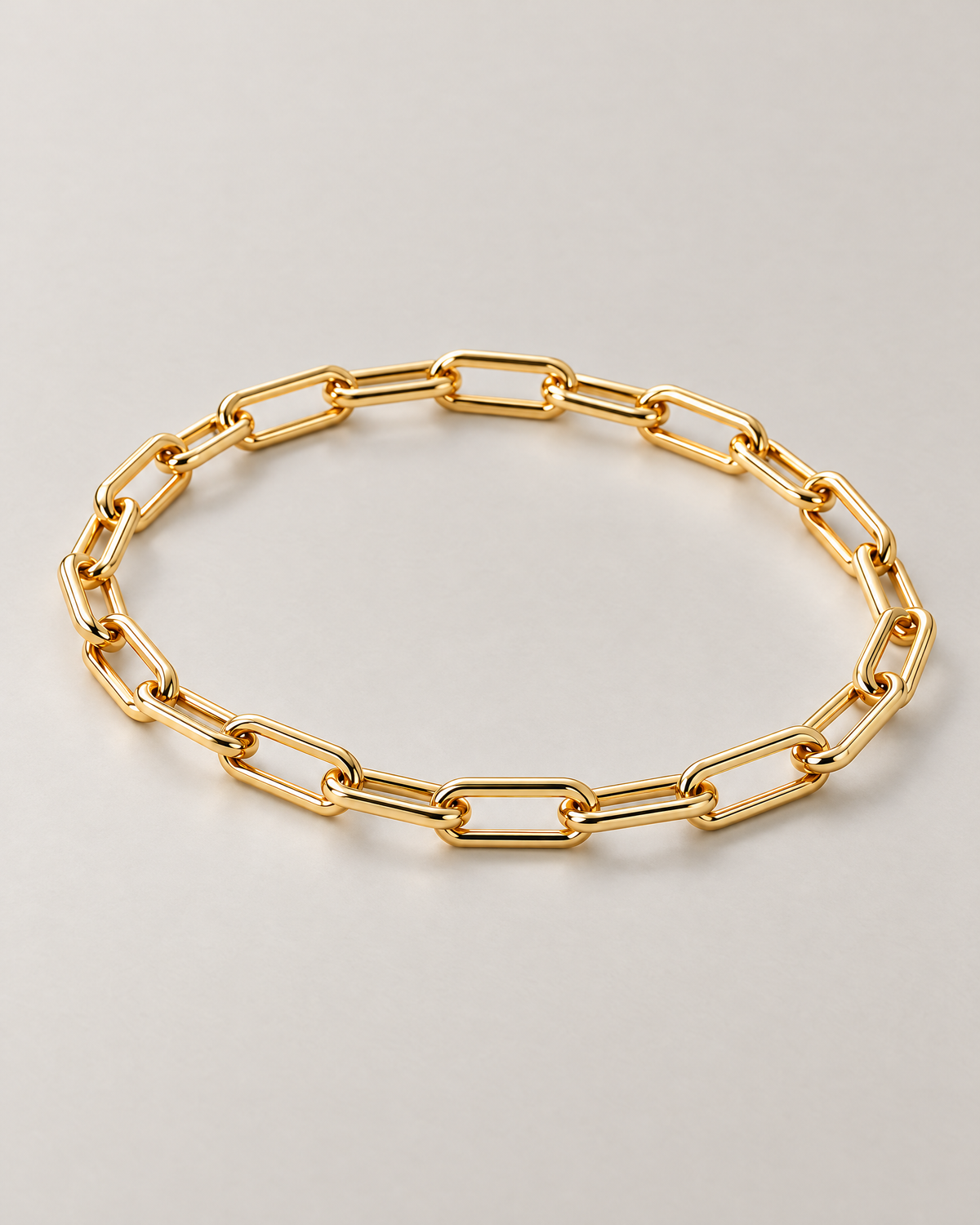 The Linnea Link Bracelet — polished gold-color oblique paperclip-link oval on pale greige — reference-based AI visualization