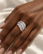 The Iona Interwoven Ring — White/silver-tone interwoven ring worn on a deep brown-skinned adult hand over ivory satin; reference-based AI visualization.