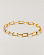 The Linnea Link Bracelet — polished gold-color paperclip-link low-angle oval on pale greige — reference-based AI visualization