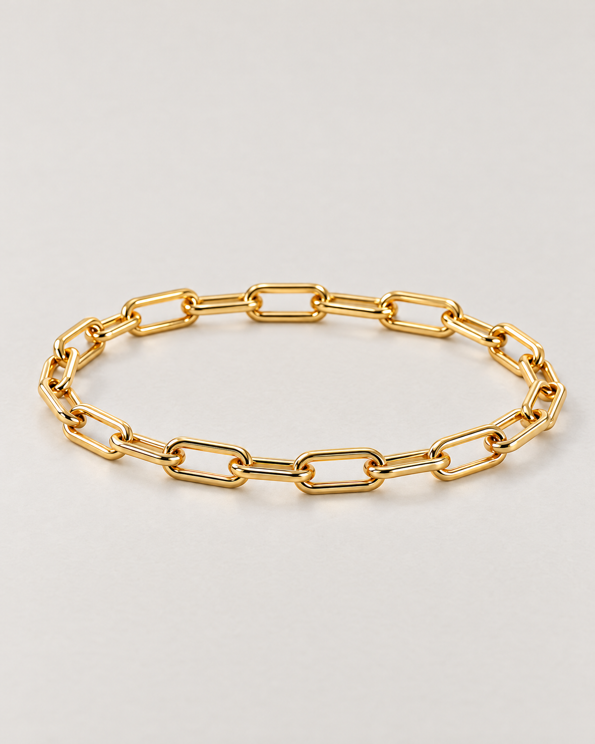 The Linnea Link Bracelet — polished gold-color paperclip-link low-angle oval on pale greige — reference-based AI visualization