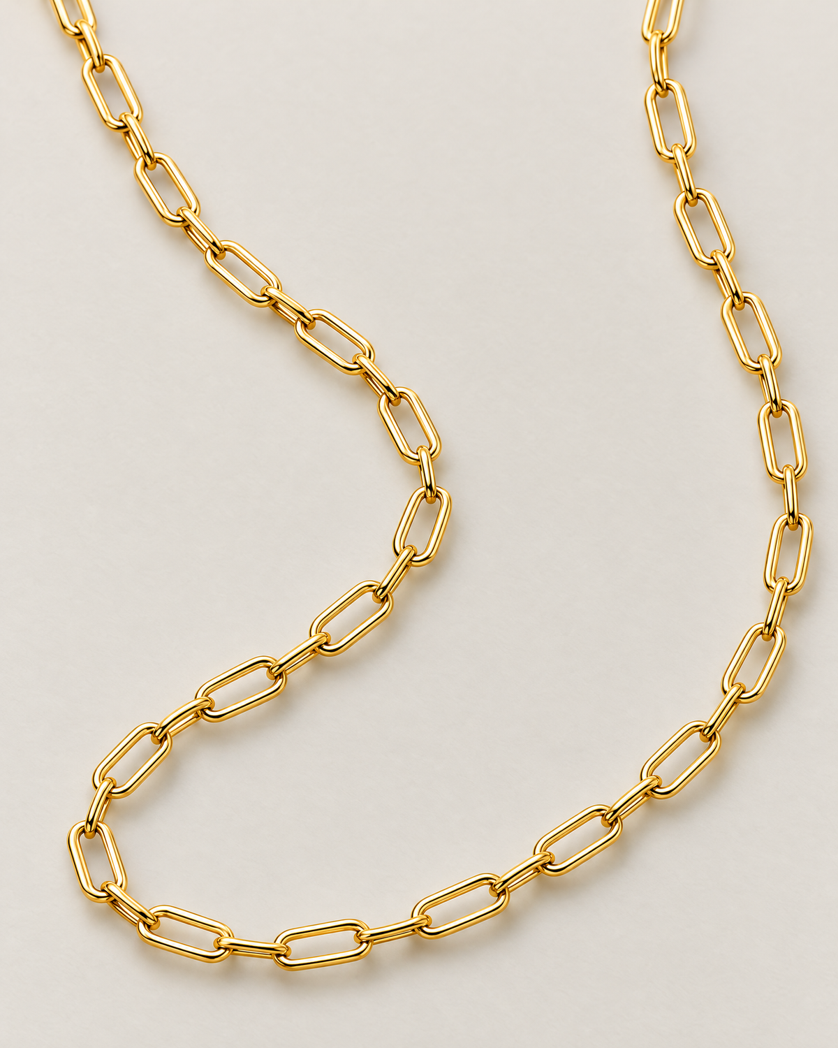 The Tova Dainty Paperclip Chain Necklace — yellow-gold-tone paperclip-link macro on pale greige, reference-based AI visualization.