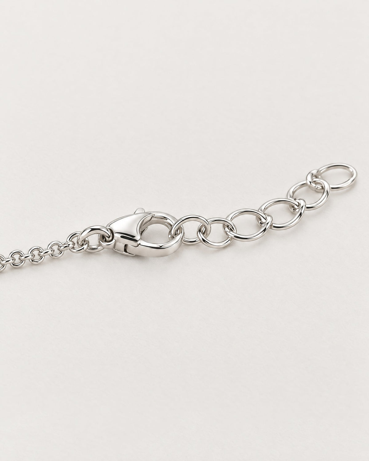 The Sora Halo Bracelet polished cool silver-tone lobster-style clasp with fine round-link chain and adjustable open oval-link extension on pale greige reference-based AI visualization