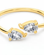 The Agnes Twin-Pear Ring in a polished yellow-gold finish with two clear pear-shaped stones, front setting macro on a pearl-white studio background — reference-based AI visualization