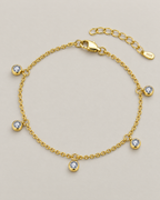 The Helle Moissanite Station Bracelet in gold tone, shown as a full five-station diagonal oval lay on pale greige, reference-based AI visualization.