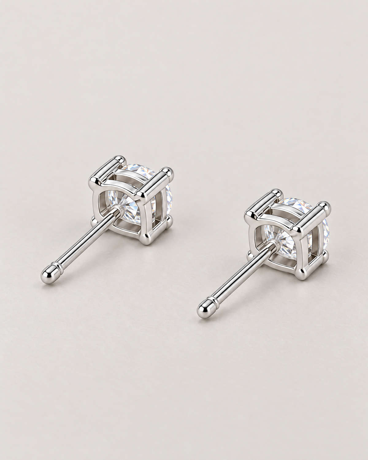The Neva CZ Stud Earrings — silver-tone rear three-quarter pair view with open setting backs, clear stones, and straight posts in a pale-greige studio; reference-based AI visualization.