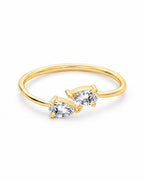 The Agnes Twin-Pear Ring in a polished yellow-gold finish with two clear pear-shaped stones, whole-ring front three-quarter product-only view on a pearl-white studio background — reference-based AI visualization