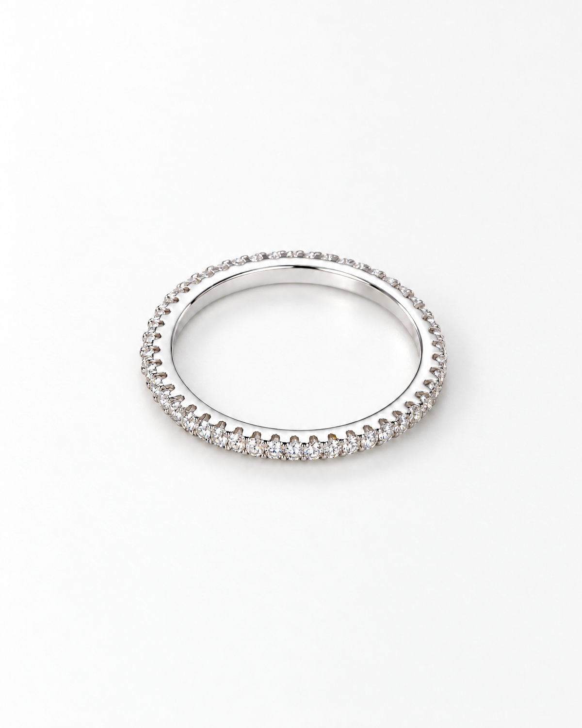 The Vale CZ Eternity Band — bright polished silver-tone clear-stone eternity band in a face-up overhead resting view on a pearl-white studio background, reference-based AI visualization