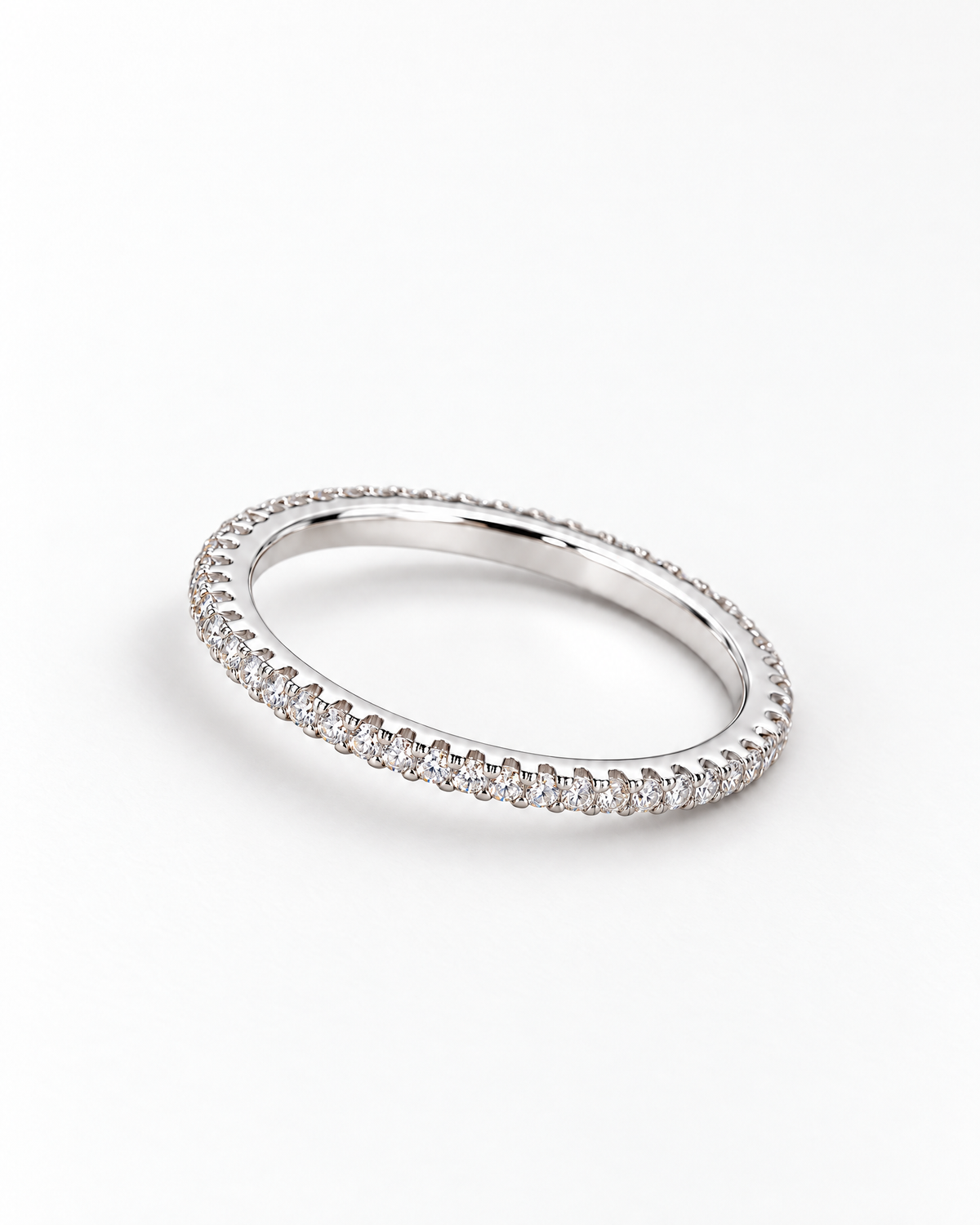 The Vale CZ Eternity Band — bright polished silver-tone clear-stone eternity band in a low resting profile on a pearl-white studio background, reference-based AI visualization