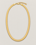 Gold-tone flat herringbone necklace in a centered closed oval with clasp and extender at the top on a pale greige studio ground; reference-based AI visualization