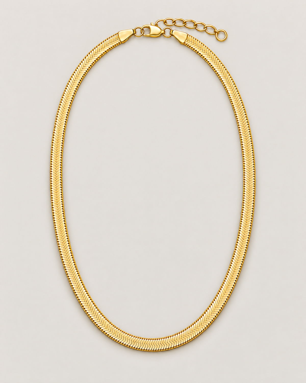 Gold-tone flat herringbone necklace in a centered closed oval with clasp and extender at the top on a pale greige studio ground; reference-based AI visualization