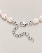 Close view of irregular off-white pearls, a silver-tone clasp and oval-link extension on a pale greige studio surface; reference-based AI visualization