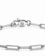 The Aelin Paperclip Bracelet in polished silver tone, macro view of the clasp with visible S925 ITALY marking and adjacent paperclip links on plain pearl-white studio background; reference-based AI visualization