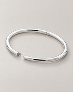 The Talo Open Cuff Bangle — polished silver-tone open oval with documented tongue-and-receiver latch and opposite hinge seam on pale greige; reference-based AI visualization