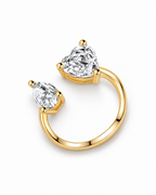 The Nessa Heart & Pear Ring in polished yellow-gold-tone metal with clear faceted heart and pear stones, shown complete in a high-angle face-up pearl-white studio view — reference-based AI visualization.