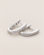The Aria CZ Hoops — offset overlapping polished silver-colored U-shaped hoops with clear round stone rows on pale greige, reference-based AI visualization
