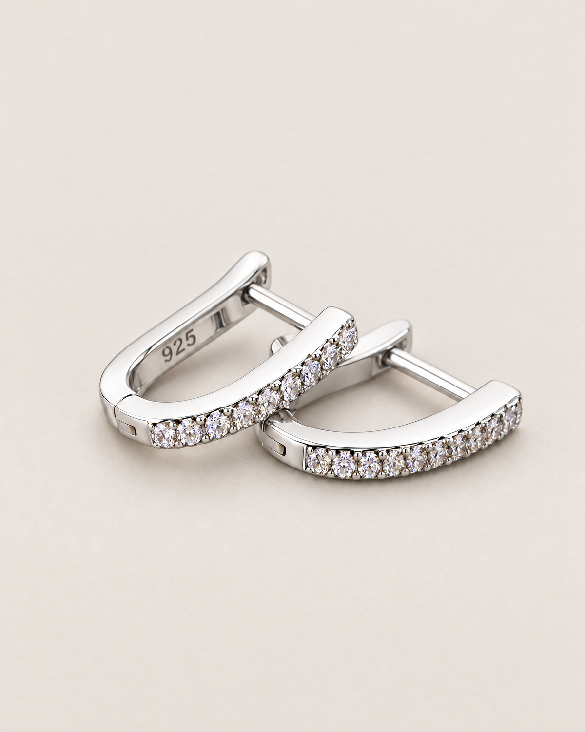 The Aria CZ Hoops — offset overlapping polished silver-colored U-shaped hoops with clear round stone rows on pale greige, reference-based AI visualization