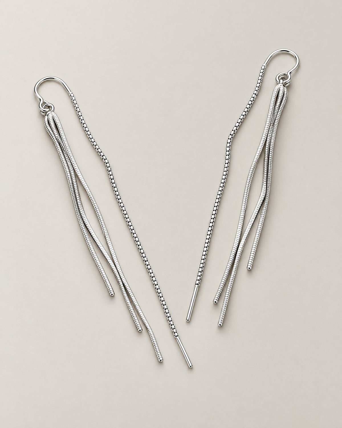 The Neri Threader Earrings, paired bright silver-tone tassel threaders in a wide V on pale greige, reference-based AI visualization