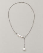 The Freya Pearl Drop Necklace — cool silver-color cable chain with three white pearl-like accent beads and a single pearl-like Y-drop on pale greige, reference-based AI visualization