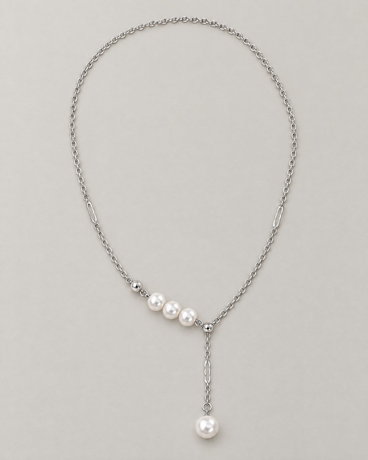 The Freya Pearl Drop Necklace — cool silver-color cable chain with three white pearl-like accent beads and a single pearl-like Y-drop on pale greige, reference-based AI visualization