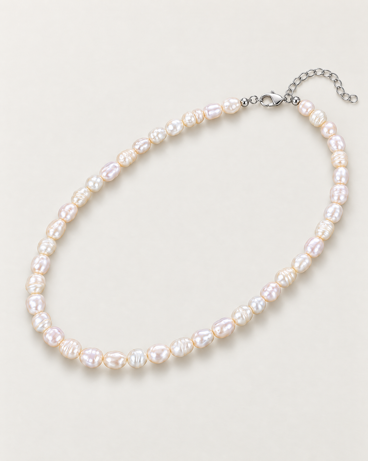 Irregular off-white pearl strand in a complete diagonal oval with clasp and extension at upper right on a pale greige studio surface; reference-based AI visualization