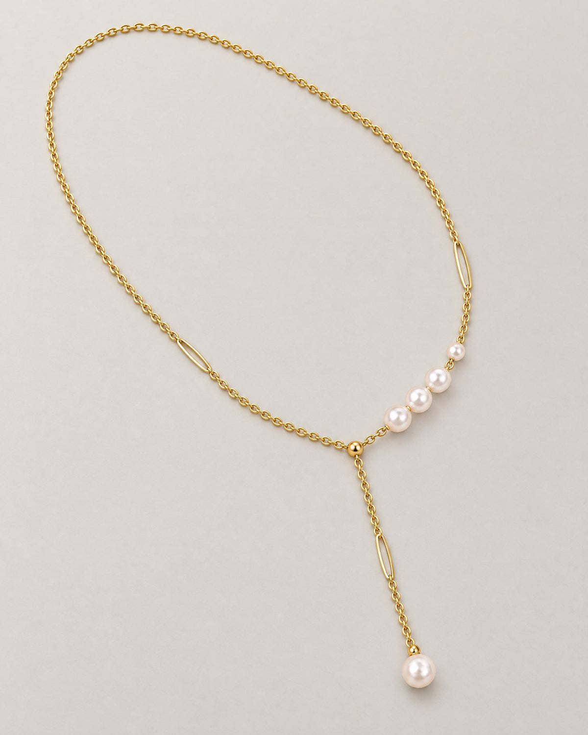 The Freya Pearl Drop Necklace — warm gold-tone cable chain with asymmetric white pearl-like accent beads and a single pearl-like Y-drop on pale greige, reference-based AI visualization
