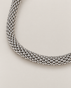 The Liva Mesh Chain Bracelet silver-tone woven mesh in a curved macro composition on warm pale greige; reference-based AI visualization.