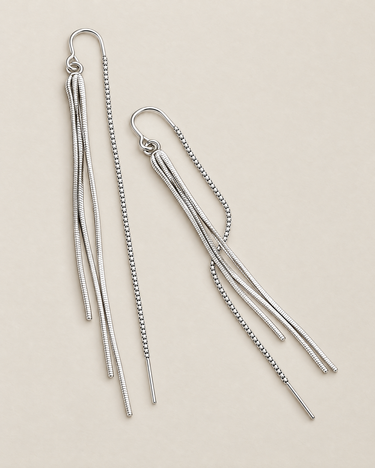 The Neri Threader Earrings, paired bright silver-tone vertical and diagonal tassel threaders on pale greige, reference-based AI visualization