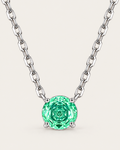 Round green faceted pendant in a silver-colored four-prong setting with a balanced linked-chain U on a pale greige studio ground — reference-based AI visualization