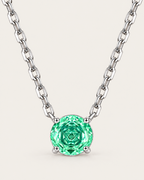 Round green faceted pendant in a silver-colored four-prong setting with a balanced linked-chain U on a pale greige studio ground — reference-based AI visualization