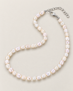 Irregular off-white pearl strand flowing in an asymmetrical open loop with visible clasp and extension on a pale greige studio surface; reference-based AI visualization